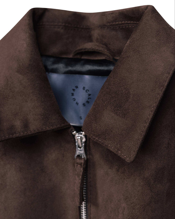 Close-up of a dark brown suede jacket collar with a silver zipper and a visible inner neck label reading Human Scales.